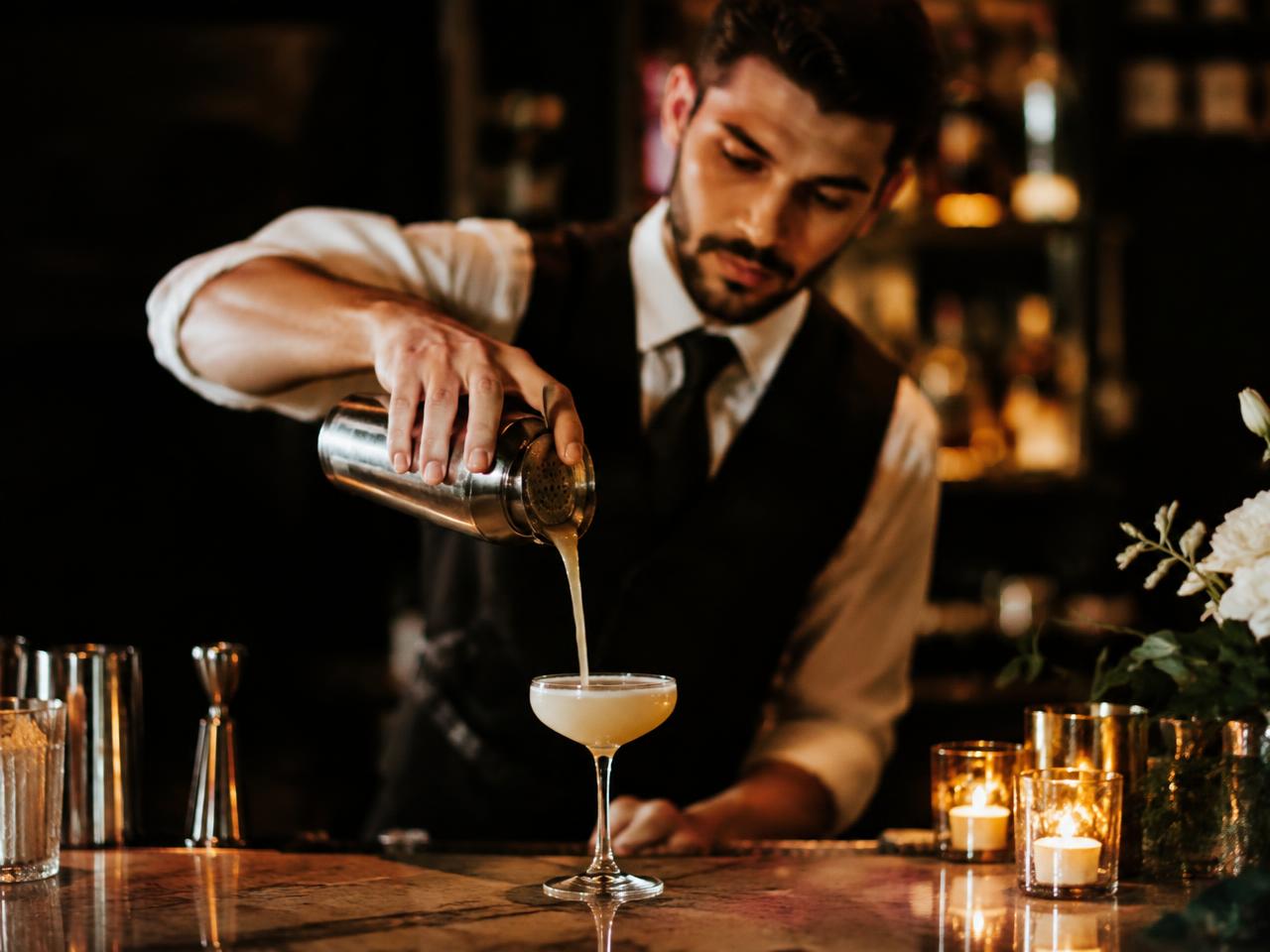 A bartender pouring a cocktail at a candlelit event bar
